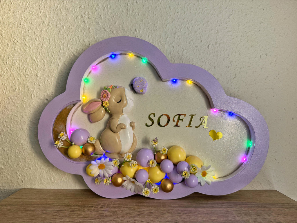 Decorative cloud-shaped plaque with cartoon characters, colorful balls, and the name 'SOFIA' on a light background.