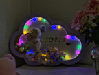 Decorative cloud-shaped plaque with LED lights, teddy bear, and 'SOFIA' text on a dark background.